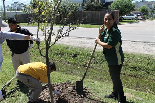 Ms. Vasquez smiling next to her recently planted tree.